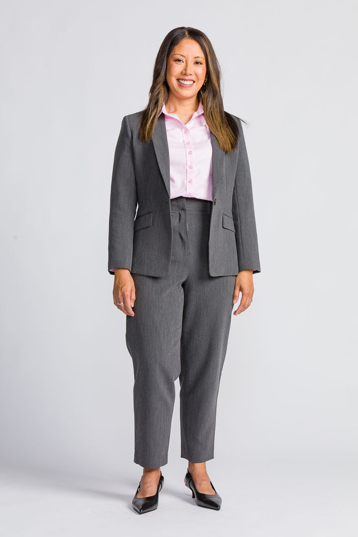 Woman wearing a gray suit with a pink tailored shirt on a white background